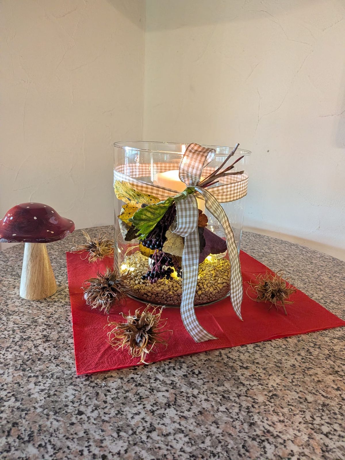 Herbstliches Tischgesteck mit Windlicht auf rotem Tischläufer