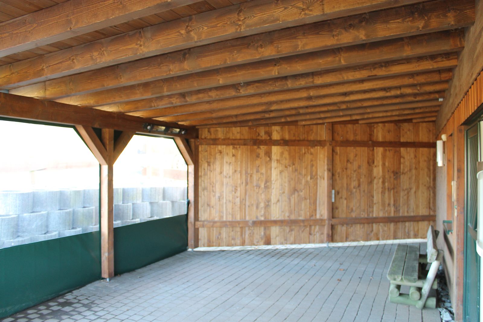Weiter Blick in den überdachten Unterstand mit Holzbalken und Pflaster