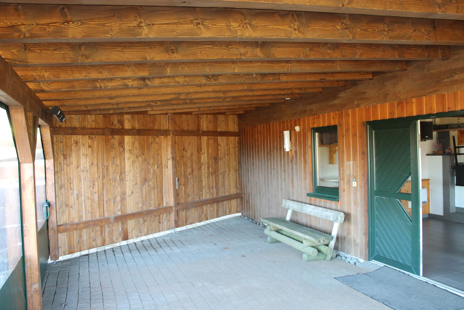 Unterstand mit Holzbank und Zugang zum Innenraum der Hütte